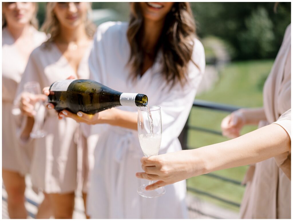 bride pouring a bridesmaid a glass of champagne on the balcony at Bear Brook Valley