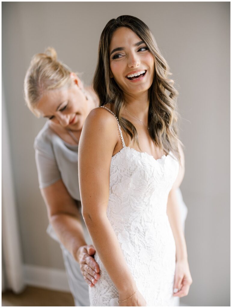 bride getting zipped up in her white lace wedding dress while smiling