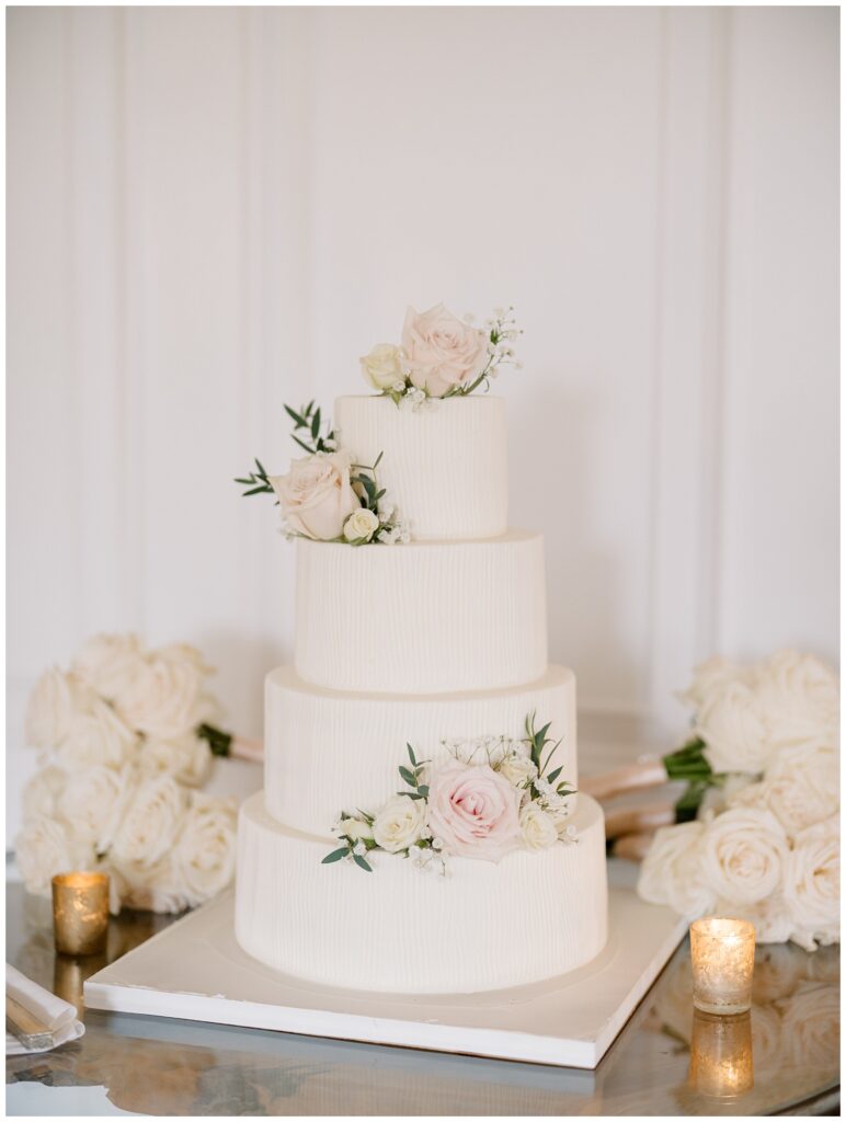 white four tiered cake decorated with white and pink roses 