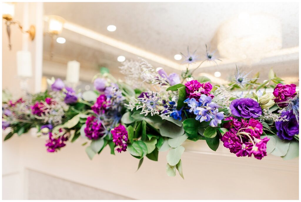 purple, blue and pink flowers adorning the fireplace at wedding reception