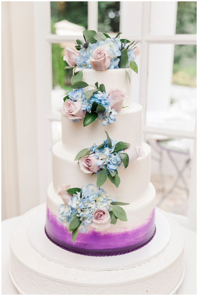 white wedding cake topped with pink roses and blue hydrangeas
