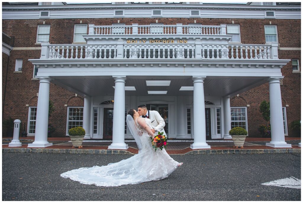 groom dipping back bride for kiss in front of The Molly Pitcher Inn venue