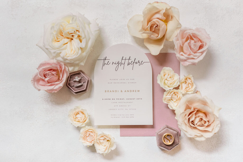 pink and ivory invitation and envelope surrounded by a ring box and flowers