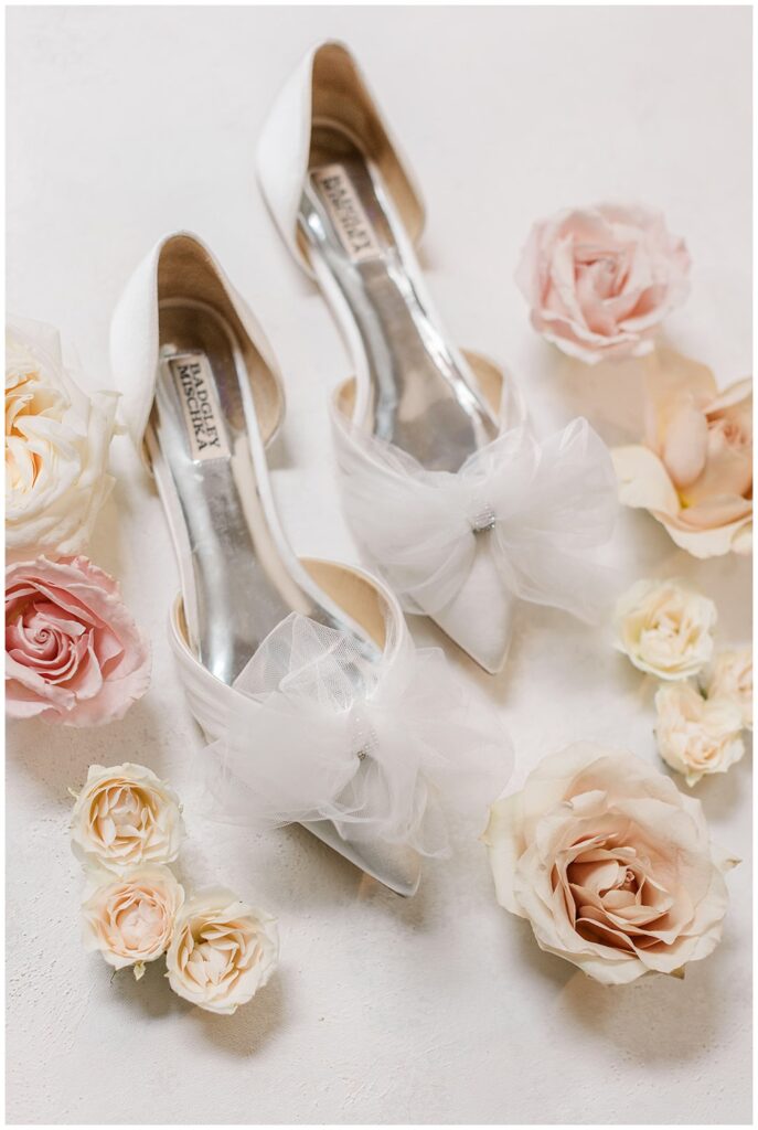 bride's Badgley Mischka white and silver wedding shoes surrounded by white and pink roses