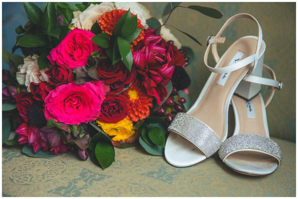 white and silver wedding shoes sitting on a chair next to a bridal bouquet
