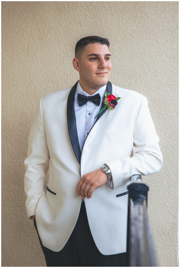 groom posing in front of a white wall while wearing a white and black tuxedo