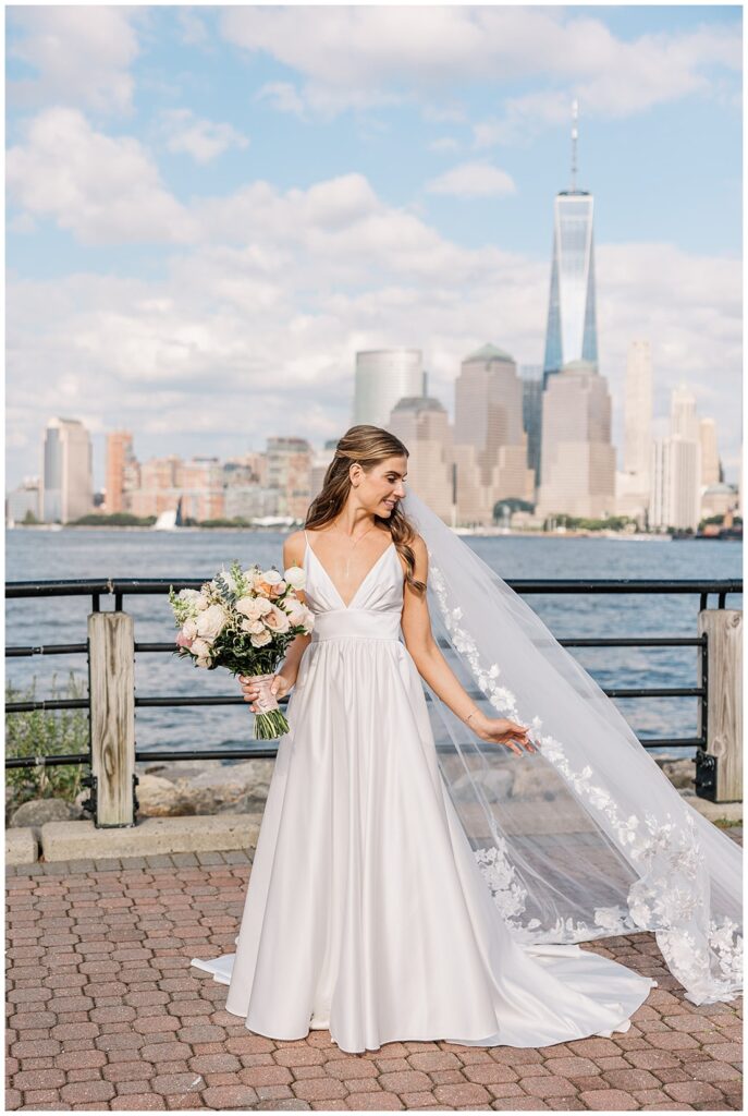 bride holding her veil and bouquet with the NYC skyline in the background