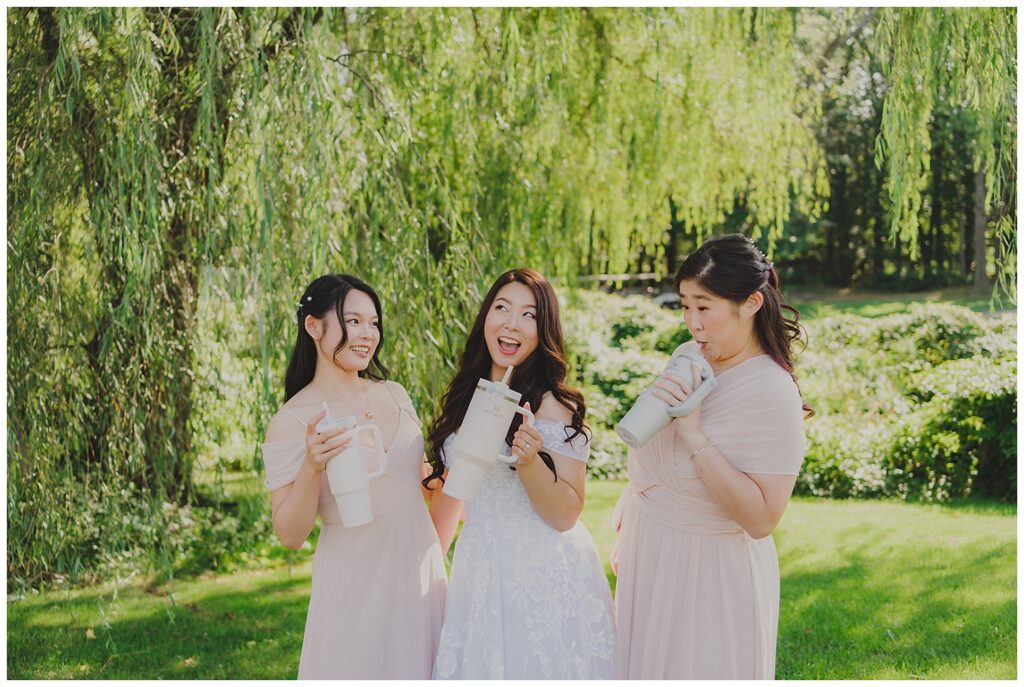 bride and bridesmaids drinking from their Stanley cups next to a willow tree