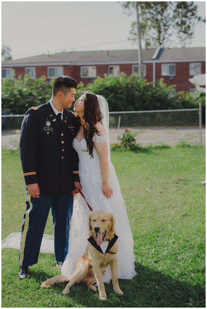 bride and groom share a kiss while posing with their dog before the wedding ceremony