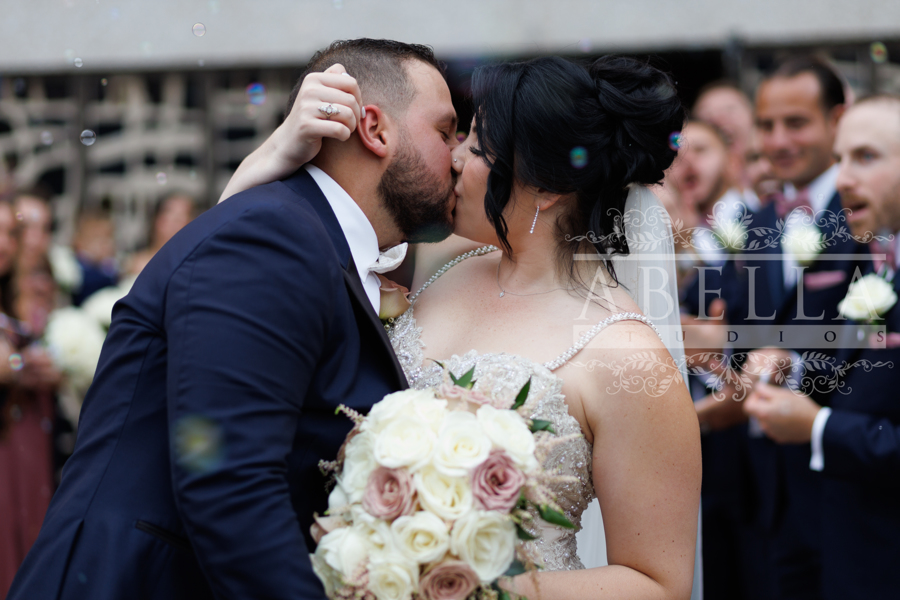 wedding couple kissing while the bridal party cheers on behind them
