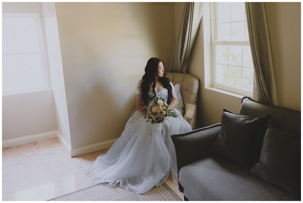 bride sitting in an arm chair looking out the window at Grand Oaks Country Club