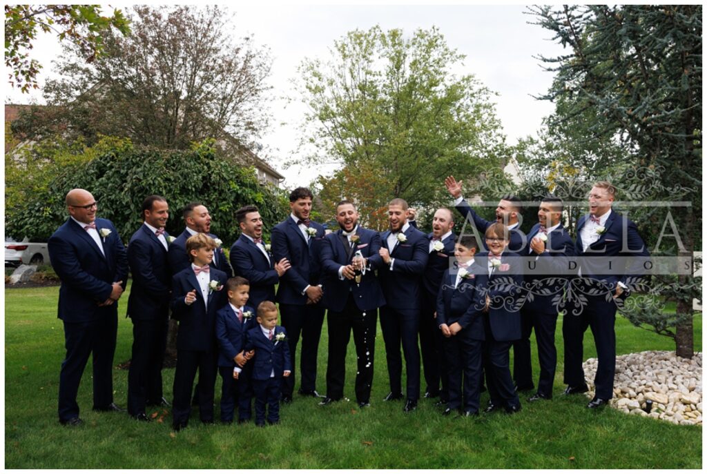 groom and groomsmen opening a bottle of champagne outside and cheering