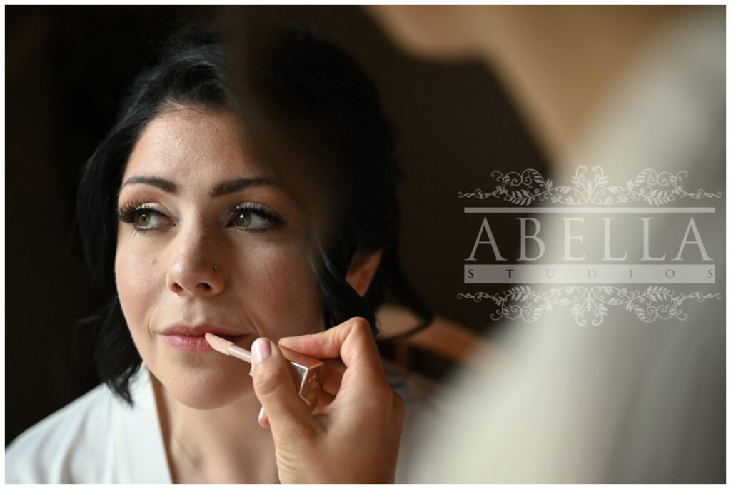 bride getting lip gloss applied while getting ready at the venue